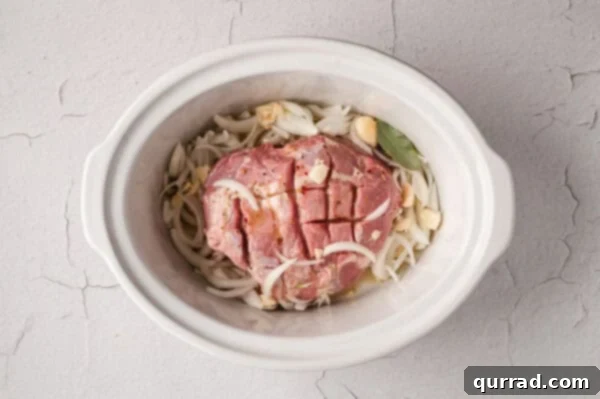 Uncooked pork shoulder in a crockpot with sliced onions and garlic.