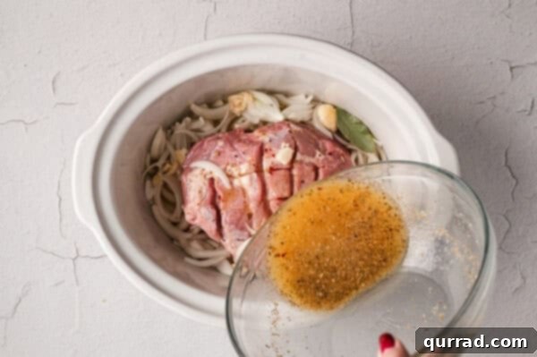 Mojo sauce being poured over uncooked pork shoulder in a crockpot.