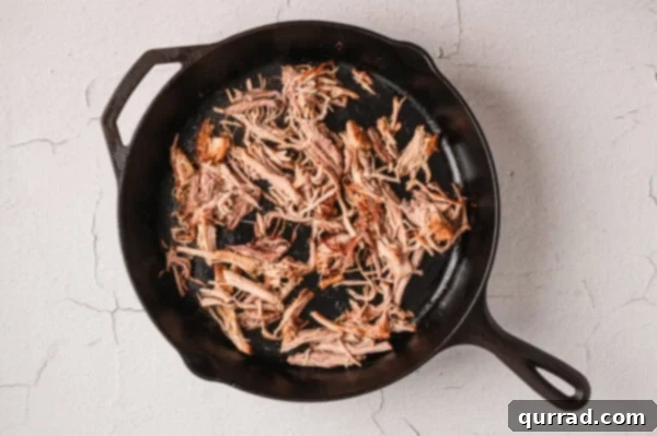 Shredded pork carnitas crisping in a hot skillet.