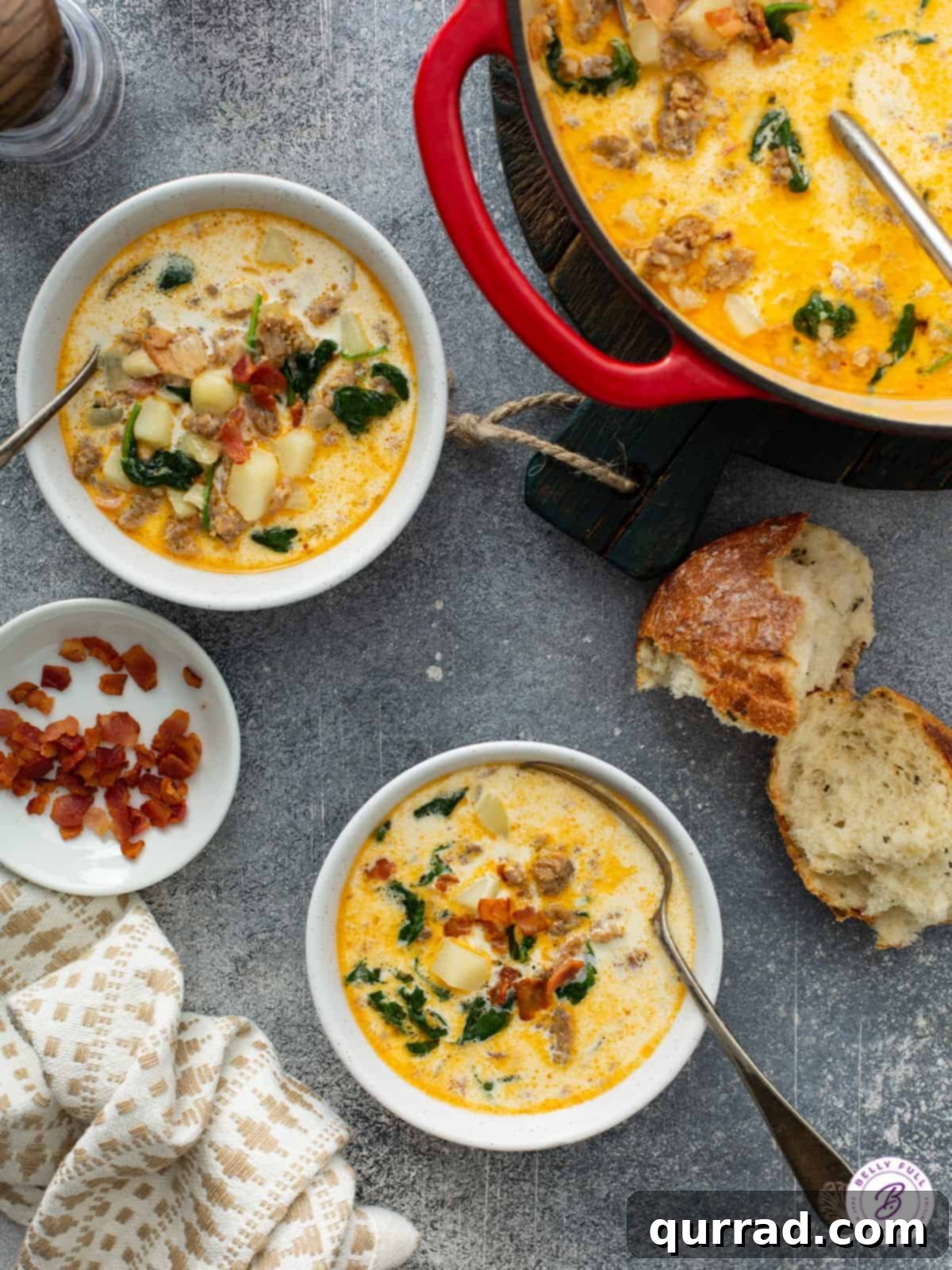 Zuppa Toscana Served with Crusty Bread Two steaming bowls of Zuppa Toscana soup on a rustic wooden table, accompanied by torn pieces of crusty bread, next to the main pot of soup.