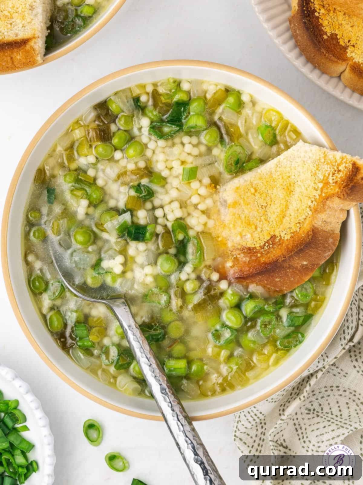 A comforting overhead view of Spring Onion and Pea Soup served in a white bowl, garnished with fresh herbs and accompanied by toasted crusty bread for dipping.