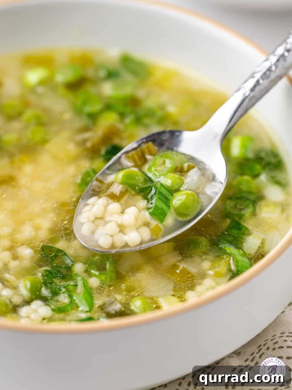 A close-up of a spoonful of Spring Onion and Pea Soup, clearly showing the tiny pasta, bright green peas, and delicate broth.