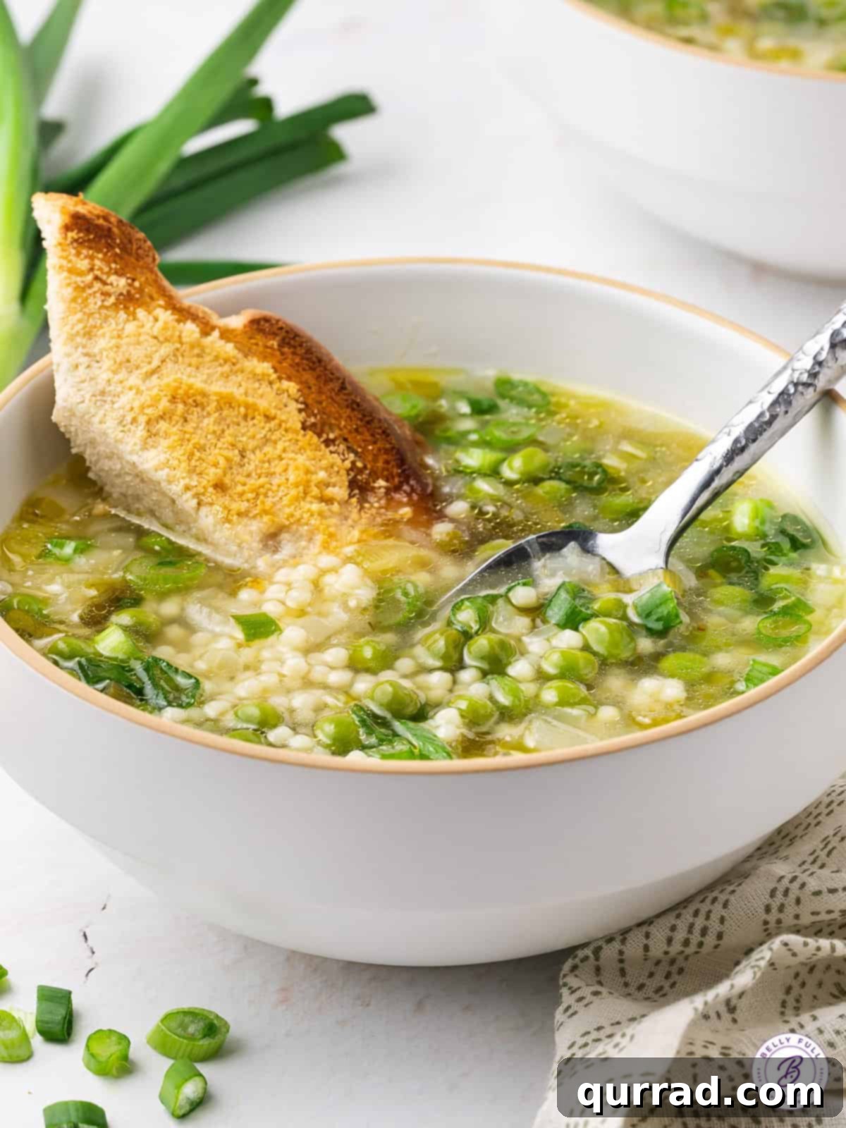A close-up shot of a bowl of Spring Onion and Pea Soup with a piece of crusty bread dipped into it, highlighting the hearty yet light consistency.