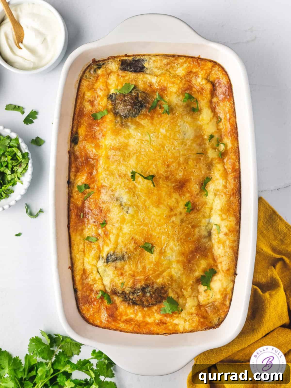 Overhead view of a golden-brown Chile Relleno Casserole in a white baking dish, ready to be served, showcasing the fluffy egg topping and melted cheese beneath.