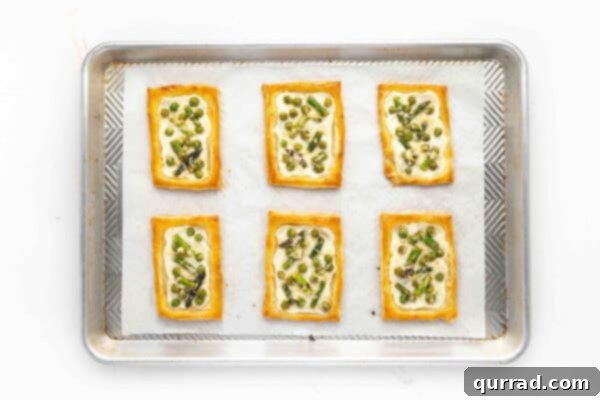 Springtime Asparagus Gems 10 Overhead view of 6 freshly baked, golden Asparagus Puff Pastry Tarts on a baking sheet.