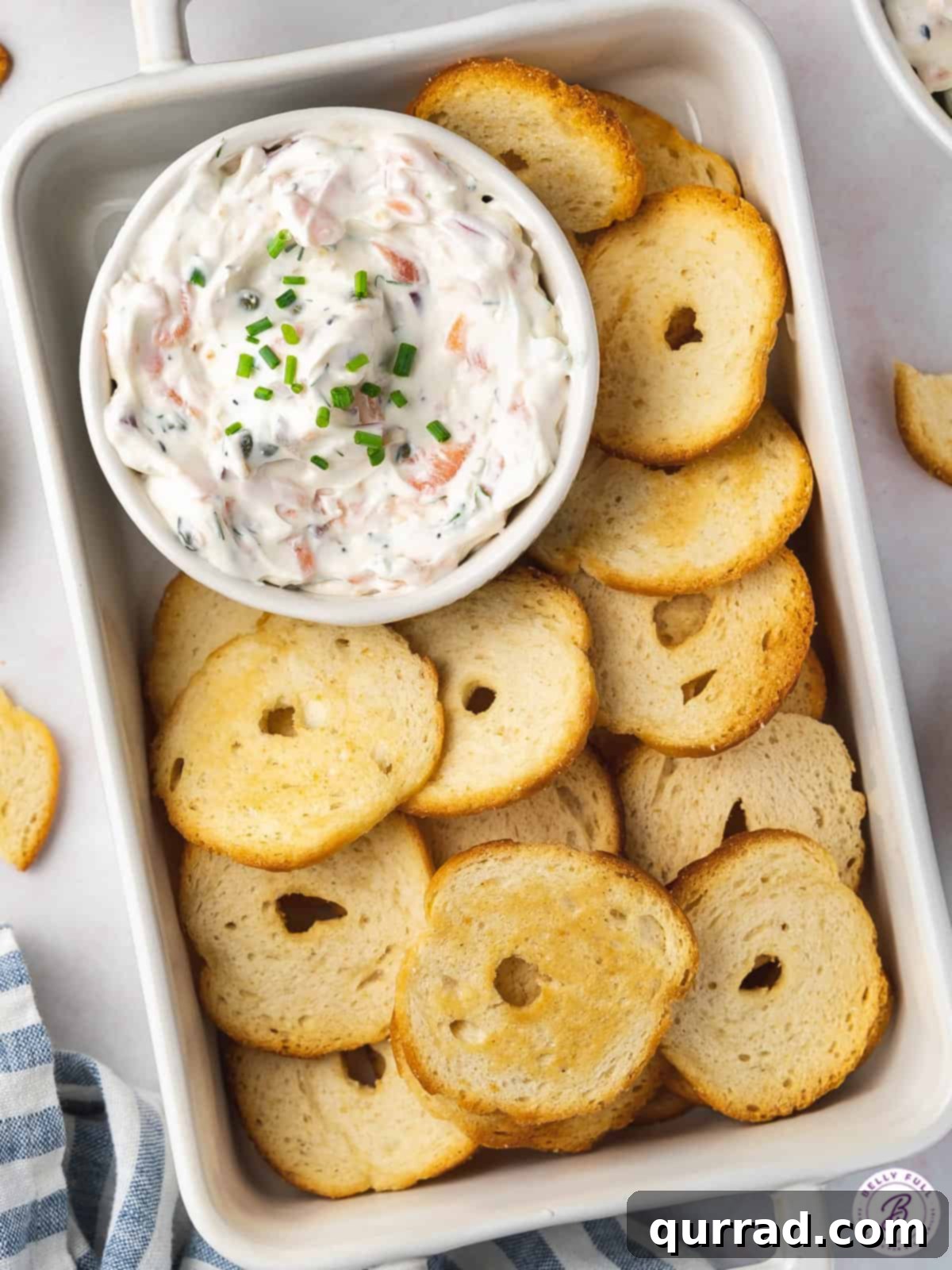 Overhead view of a bowl of creamy smoked salmon dip, beautifully garnished with fresh dill and served alongside an assortment of crispy bagel chips, ideal for sharing.