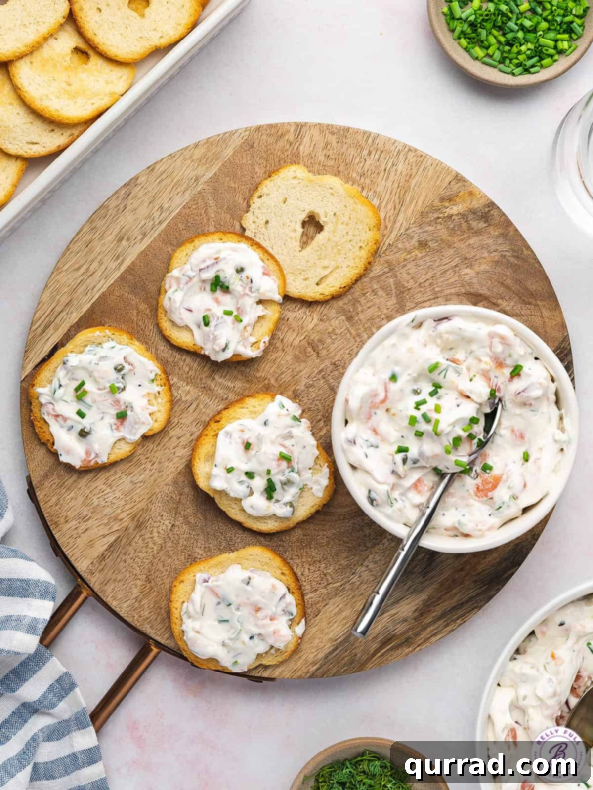 Crispy melba toast crackers topped with a generous dollop of creamy smoked salmon dip, garnished with fresh chives, arranged artfully on a wooden serving board.
