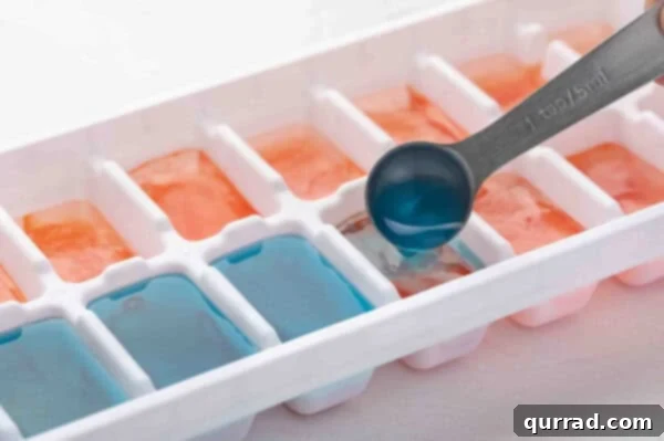 Blue liquid being poured as the final layer over red and white layers in an ice cube tray.