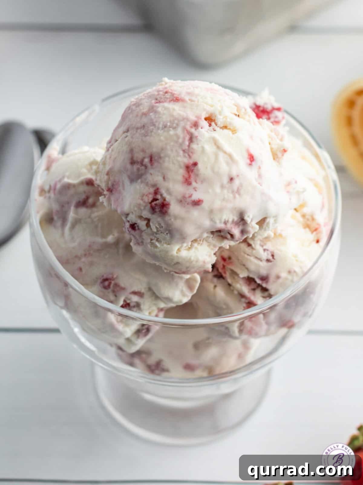 Creamy No-Churn Strawberry Delight 5 Several scoops of creamy no-churn strawberry ice cream served elegantly in a clear dessert glass, garnished with fresh strawberries.