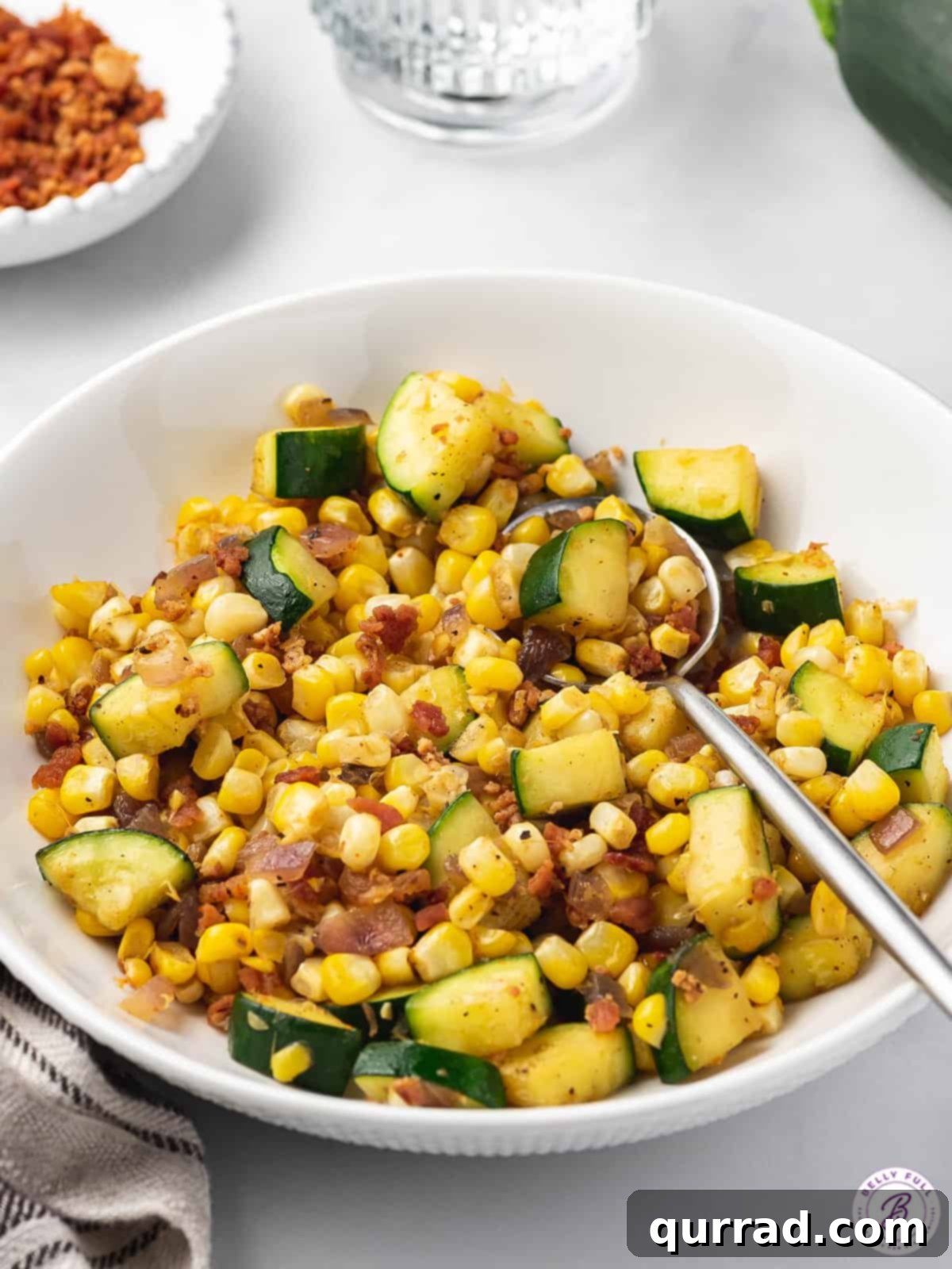 Summer Zucchini Corn Medley 5 bowl of cooked zucchini, corn, and bacon with a spoon