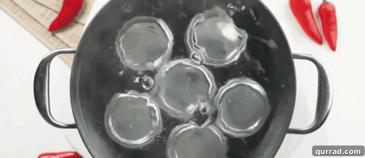 Sealed glass jars of red chili sauce submerged in a water bath canner, boiling vigorously for preservation.