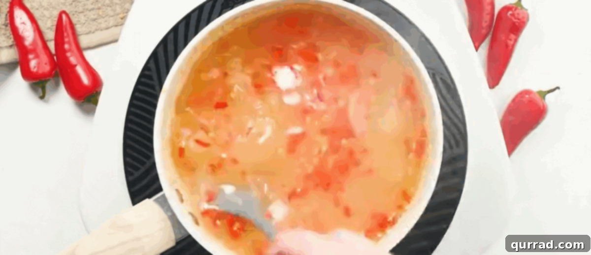 The prepared canning starch mixture being slowly poured into the vigorously stirring sweet chili sauce in a saucepan on the stovetop.