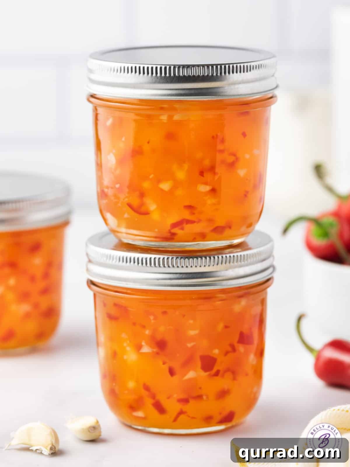 Two stacked jars of vibrant red homemade sweet chili sauce, sealed and ready for cooling or storage.