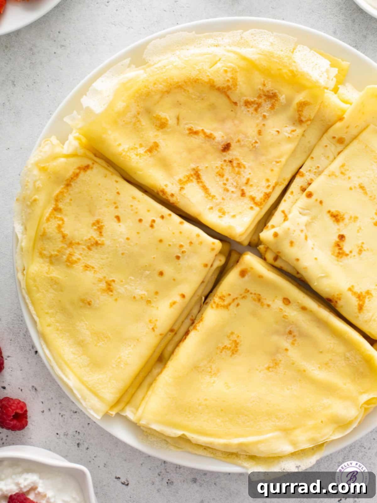 Four stacks of golden-brown, folded crepes on a rustic plate, ready to be filled.