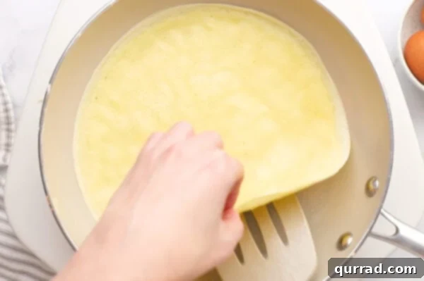 A crepe being gently flipped in a frying pan with a spatula.