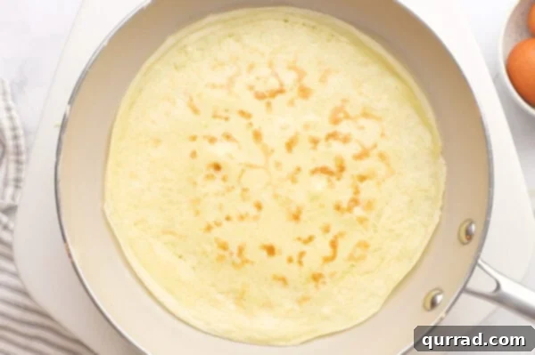 A golden-brown crepe sizzling gently in a frying pan after being flipped.