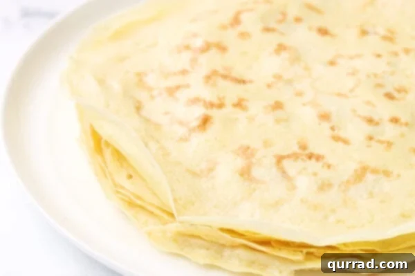 A beautiful stack of freshly made crepes piled on a white plate.