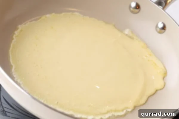 Thin layer of crepe batter evenly distributed across the bottom of a frying pan by swirling.