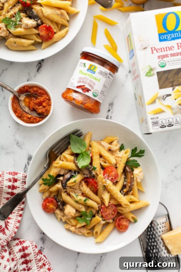 cooked penne pasta with sun dried tomato pesto in white bowl, garnished with fresh parsley