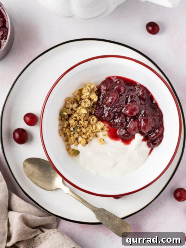 Sweet and Tart Homemade Cranberry Sauce 5 A rustic bowl of homemade cranberry sauce paired with creamy yogurt and crunchy granola, suggesting a healthy and delicious breakfast option.