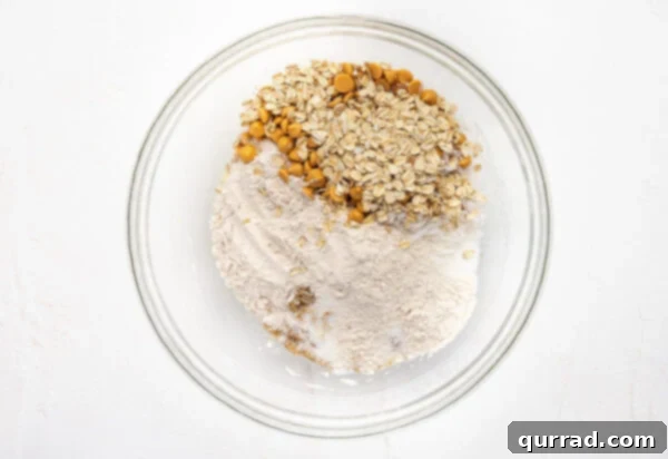 Layers of Cookie Joy 10 Dry cookie mix ingredients added to wet ingredients in glass bowl