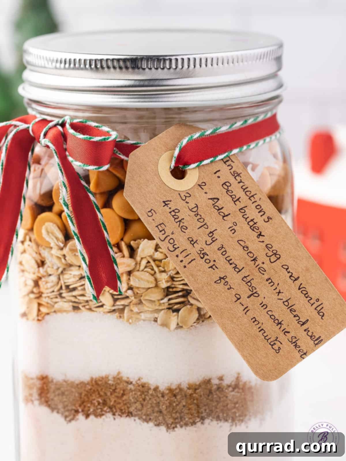 Layers of Cookie Joy 4 Layered cookie mix in a glass jar, adorned with a decorative ribbon and a gift tag containing baking instructions.