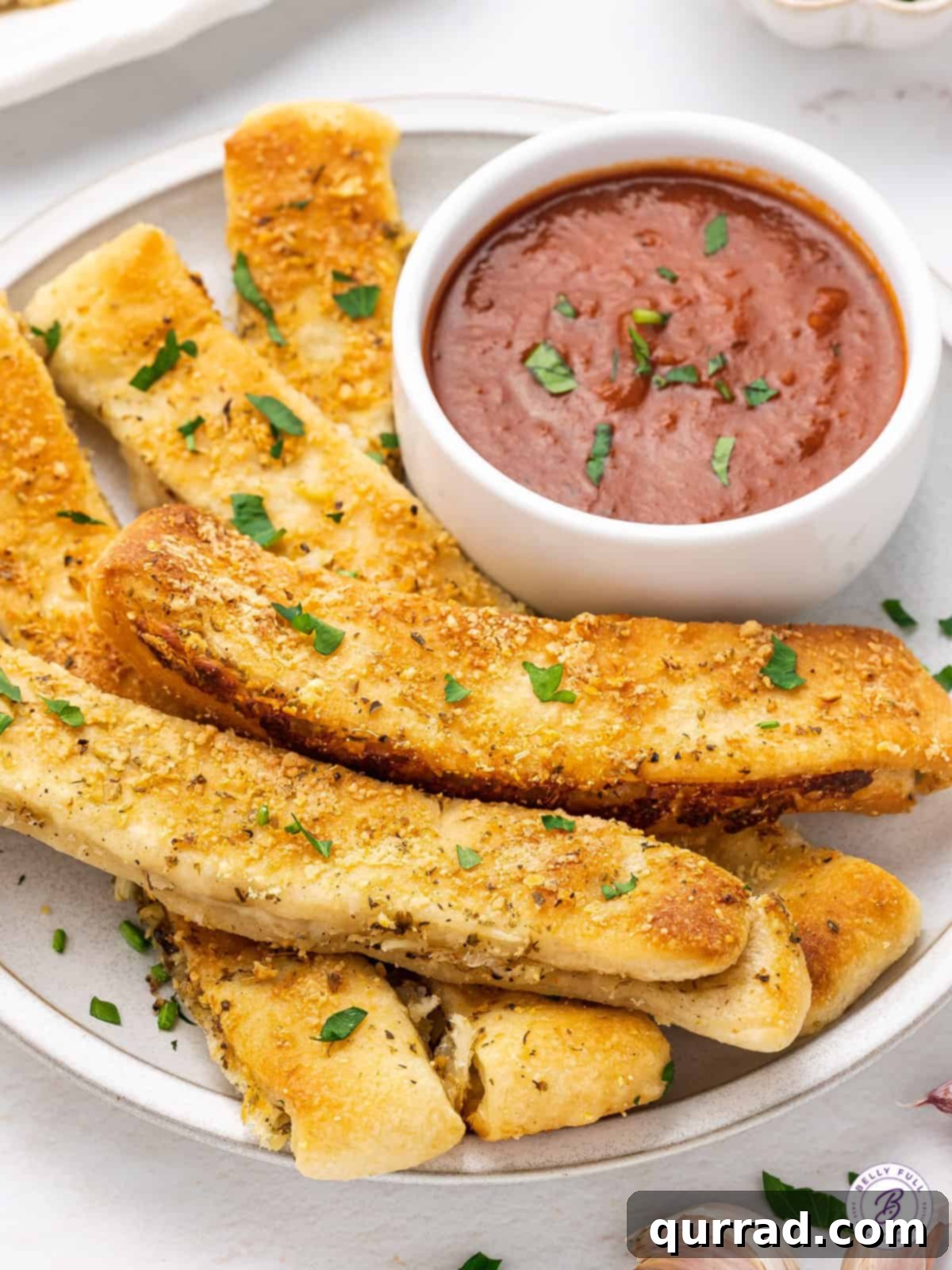Effortless Skillet Breadsticks 5 Delicious baked cheesy breadsticks on a white plate, served with a small bowl of marinara sauce for dipping.