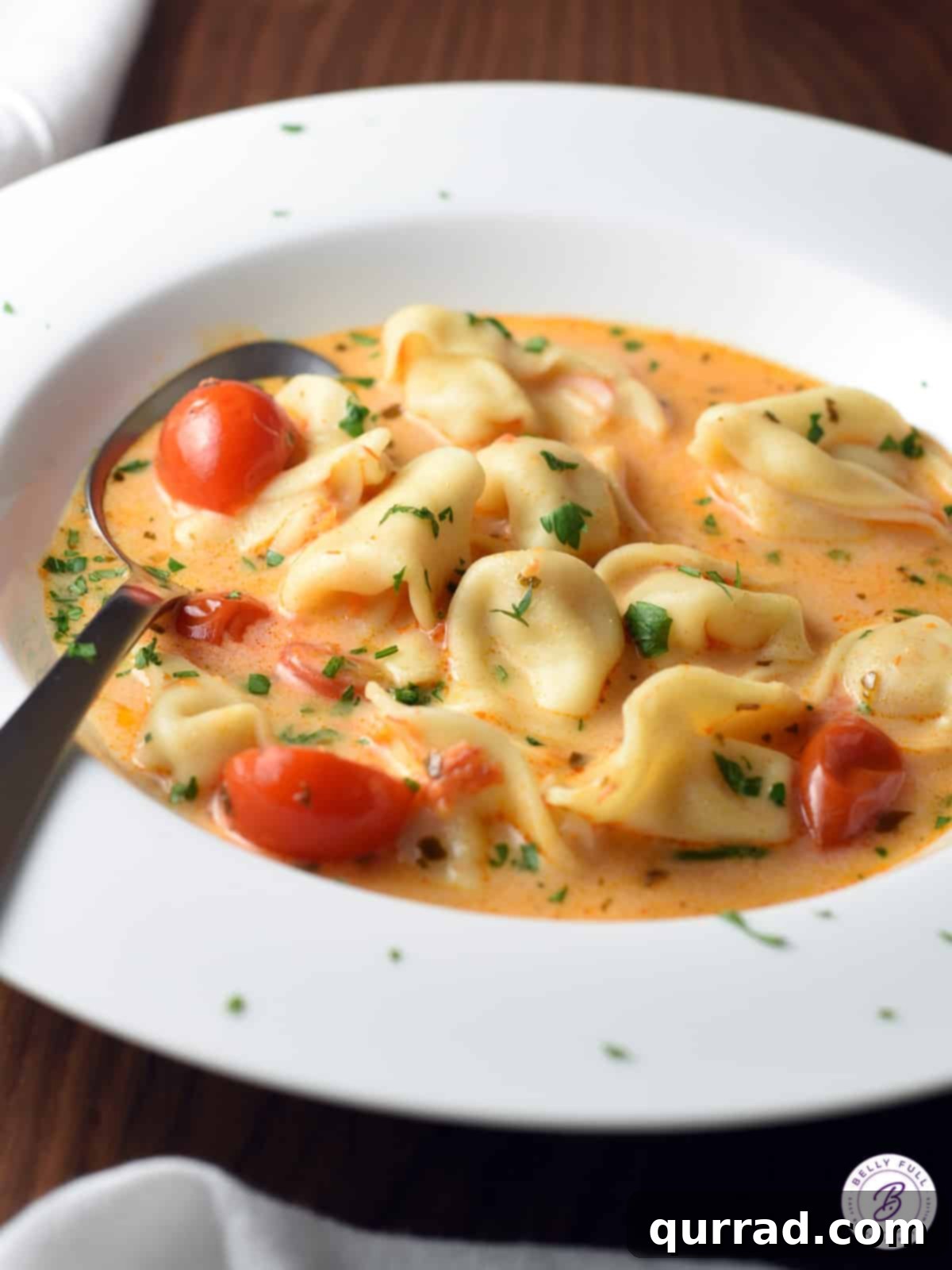 Tomato tortellini soup in a white bowl with a spoon.