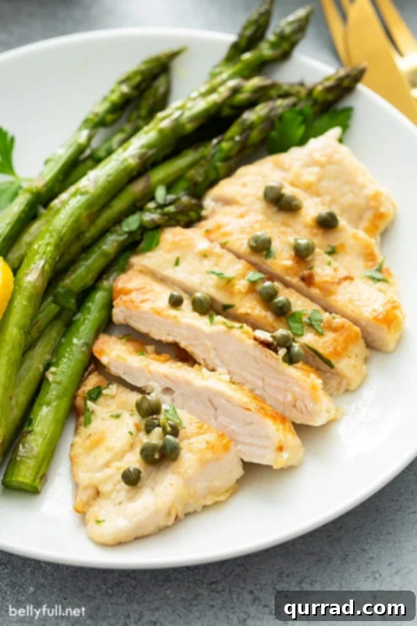20 Minute Chicken Piccata 3 Beautifully sliced chicken piccata, showcasing its tender interior and rich sauce, arranged on a white plate with lemon slices.
