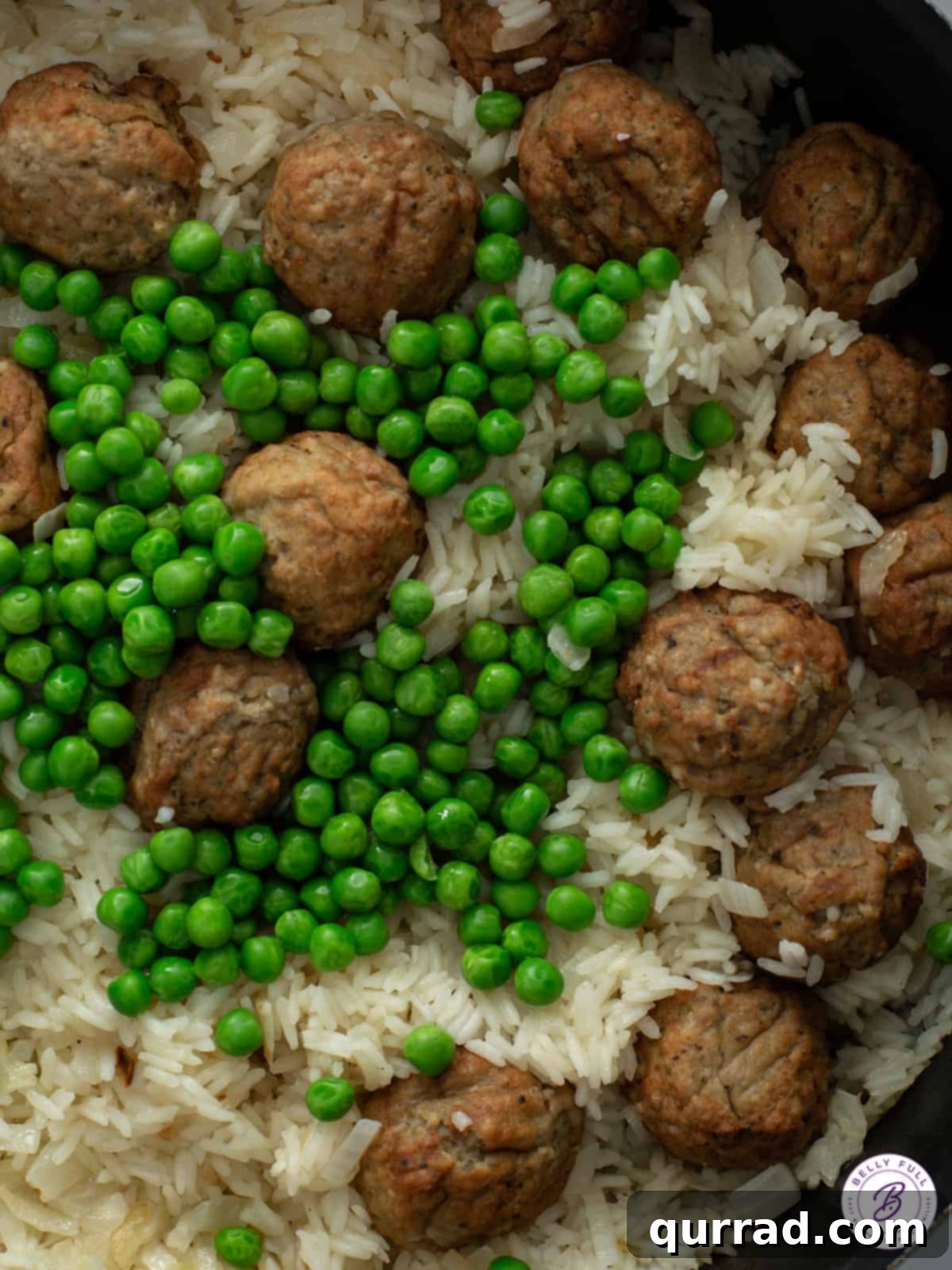 Close-up shot of the Meatball Rice Skillet in a pan, showing the juicy meatballs, perfectly cooked rice, and bright green peas mixed together, steam gently rising.