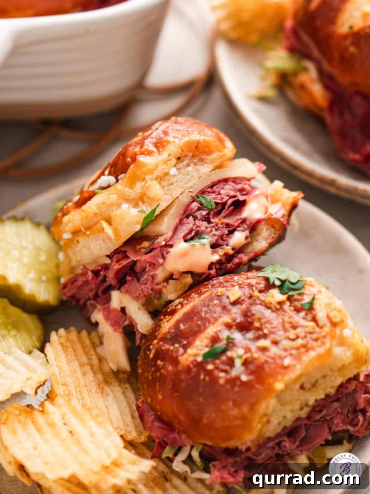 Irresistible Pretzel Reuben Sliders 13 close up Reuben Pretzel Sliders on plate with chips and pickles, ready to eat