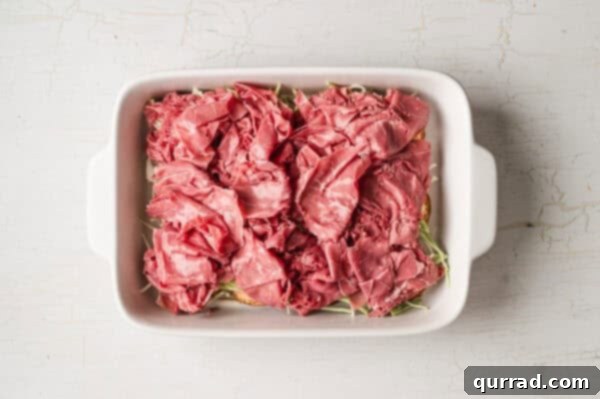 bottom buns in casserole dish with thousand island dressing, shredded cabbage, and sliced corned beef