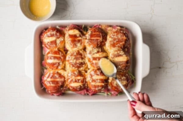 unbaked assembled pretzel bun sliders in casserole dish with spooned melted butter