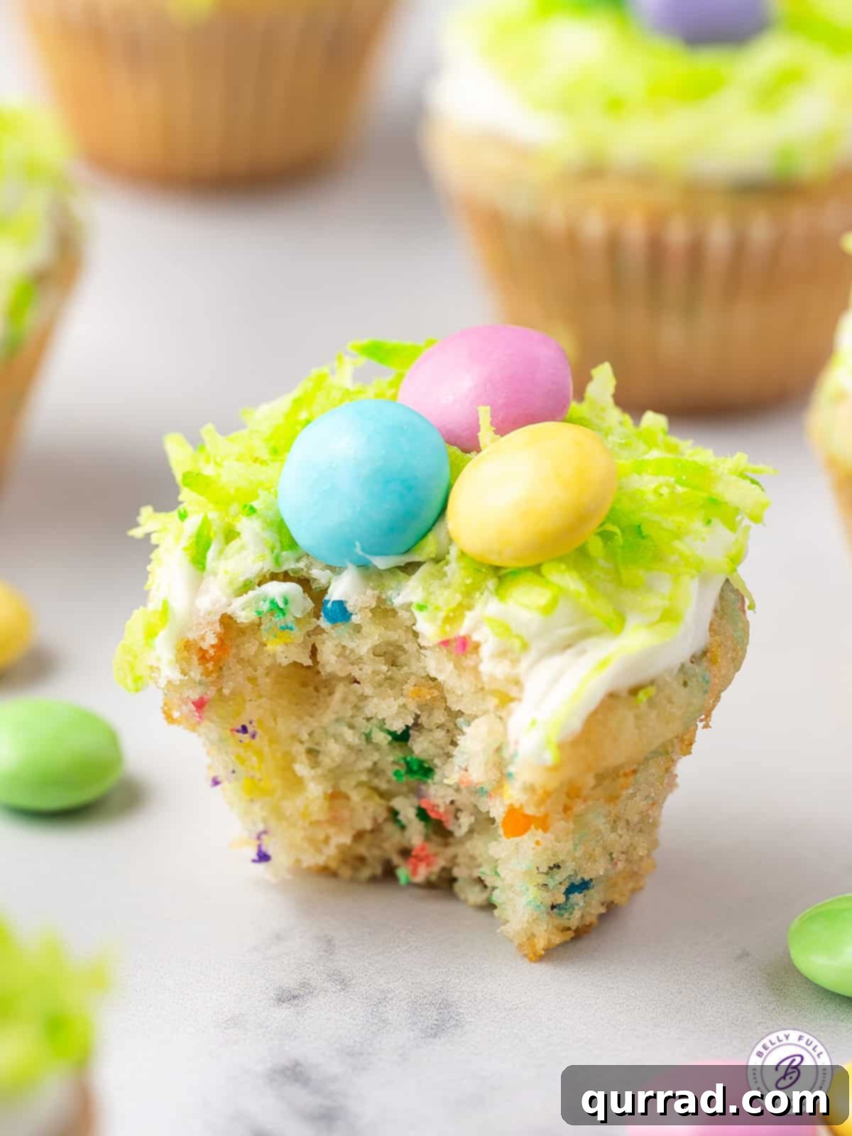 Hoppy Easter Mini Sprinkle Cupcakes 5 A close-up of a Mini Funfetti Easter Cupcake with a bite taken, highlighting the moist interior and festive decorations.
