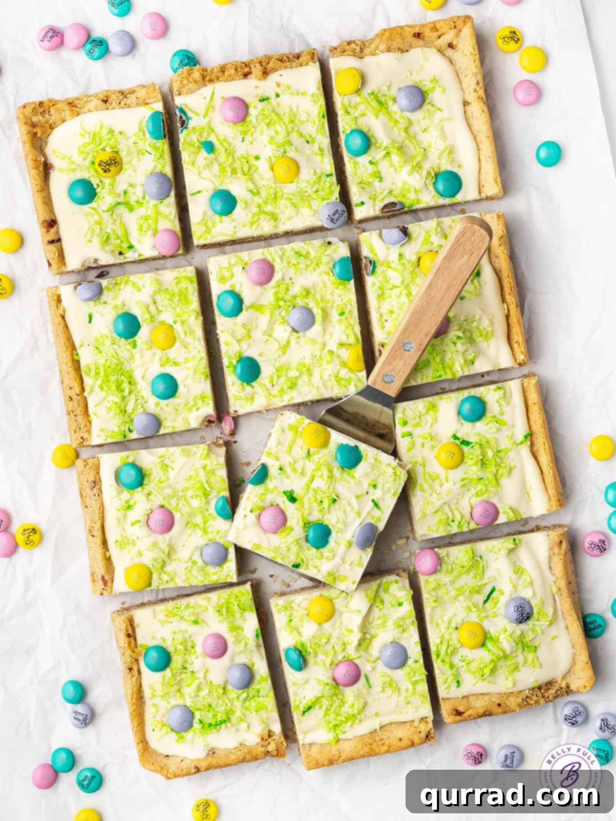Overhead view of freshly cut Easter Sugar Cookie Bars arranged on parchment paper, showing layers of cookie, chocolate, coconut, and M&Ms.