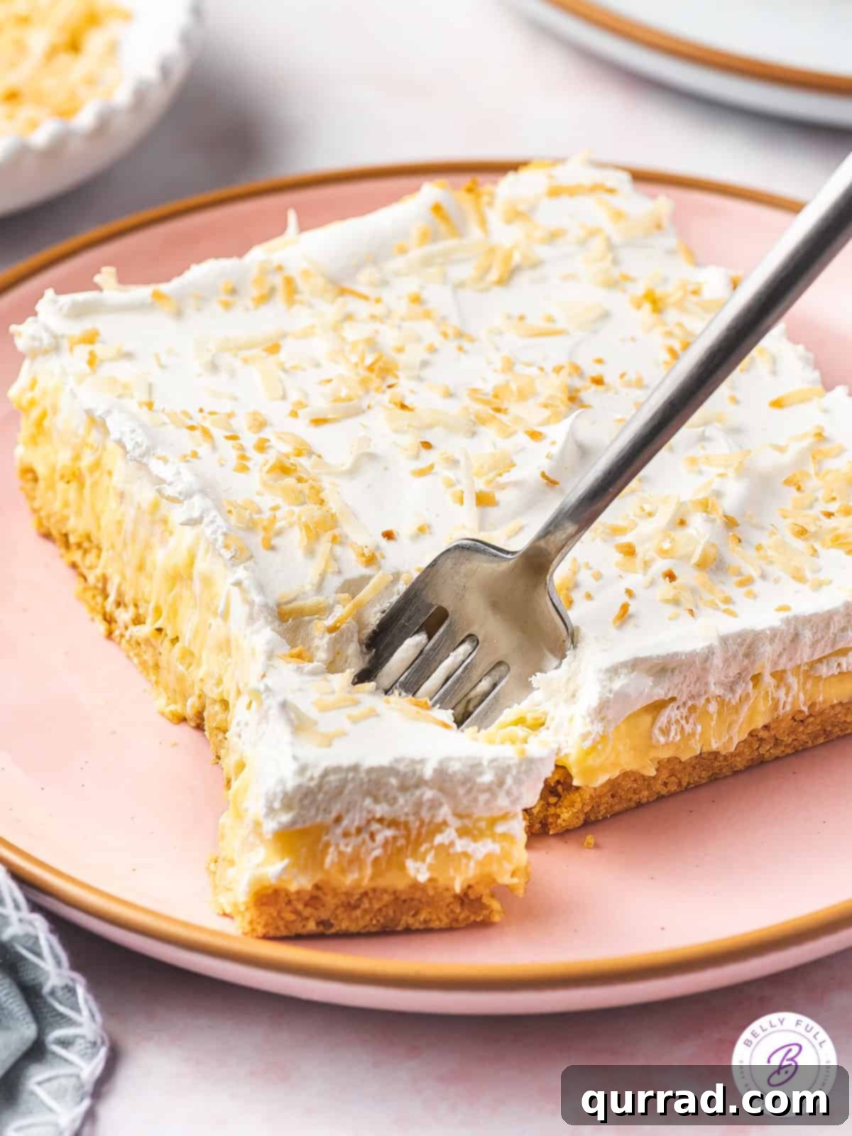 Pineapple Paradise Lush 5 A close-up of a square slice of pineapple lush dessert on a plate, with a fork holding a perfect bite, showcasing the distinct layers.