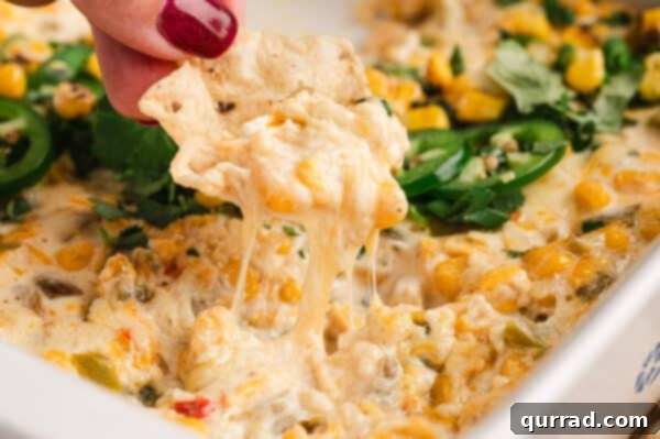 A corn chip scooping hot, cheesy corn dip from the casserole dish, ready to eat.
