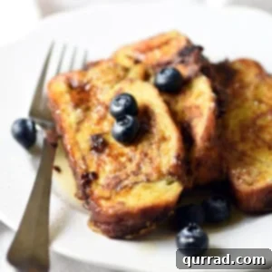 Decadent Chocolate Challah French Toast 4 Slices of chocolate French toast with blueberries on a white plate, showcasing the recipe's delicious final presentation.
