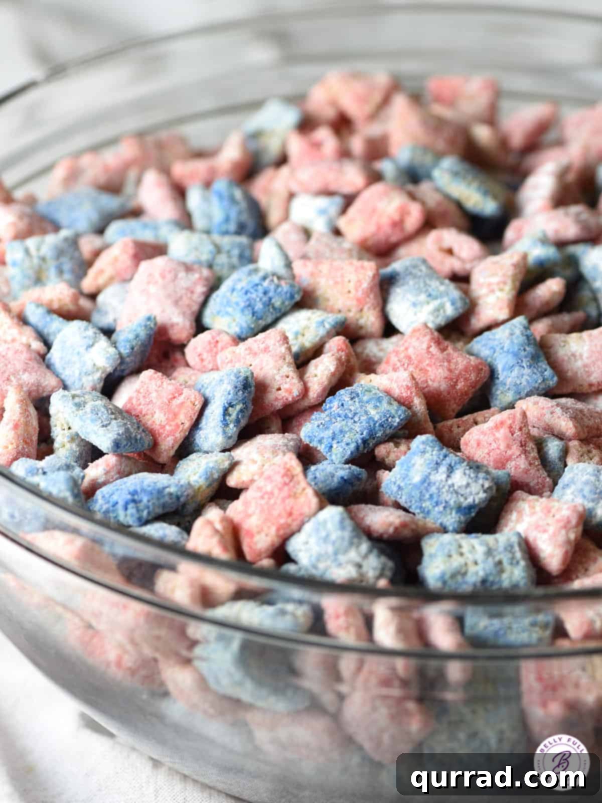 Star-Spangled Snack Mix 4 A close-up shot of a glass bowl filled with perfectly coated red, white, and blue muddy buddies, ready for a 4th of July celebration.
