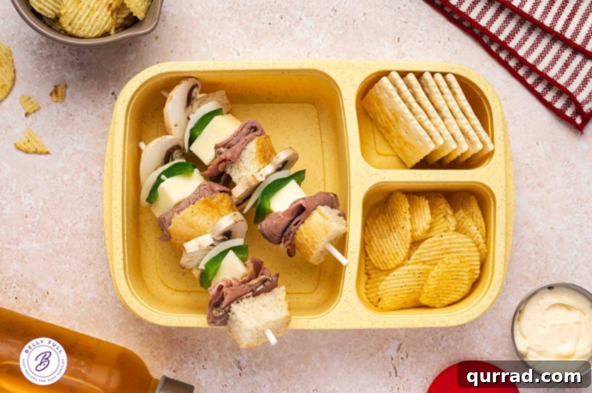 Skewered Sandwich Classics 8 Philly Cheesesteak sandwich on a stick with hoagie roll pieces, roast beef, provolone, green pepper, onion, and mushroom, presented in a lunchbox.