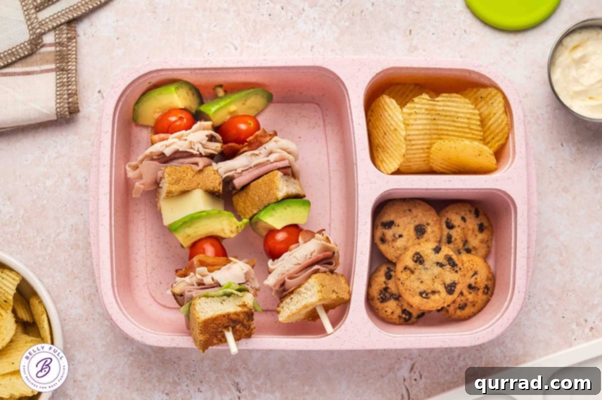 Skewered Sandwich Classics 6 Club sandwich on a stick featuring toasted white bread, iceberg lettuce, ham, turkey, bacon, tomatoes, avocado, and white cheddar in a lunch box.