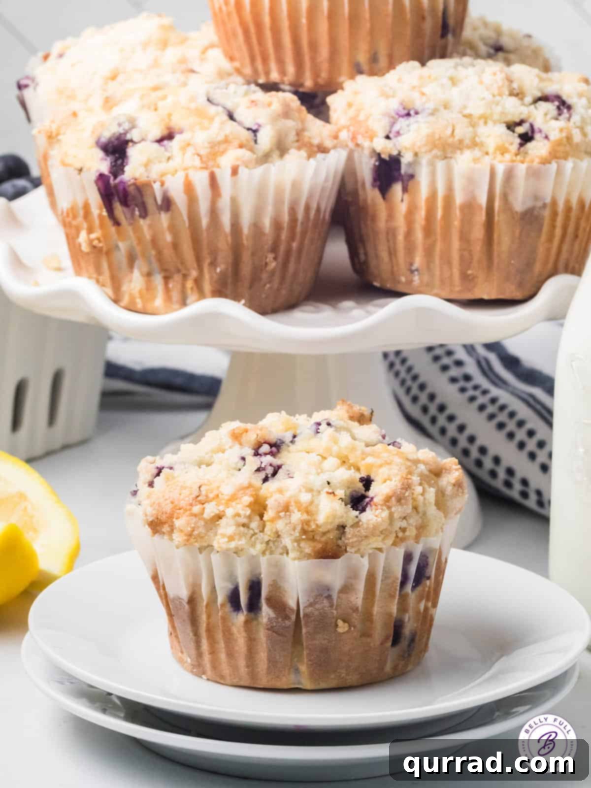 Simple Blueberry Perfection 5 Assortment of golden blueberry muffins presented beautifully on a tiered cake stand, with one muffin ready to be enjoyed on a plate.