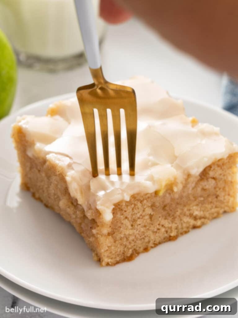Autumn Apple Caramel Slab 4 A close-up of a square piece of glazed caramel apple cake with a fork resting beside it, highlighting the smooth, sweet icing and soft cake texture.