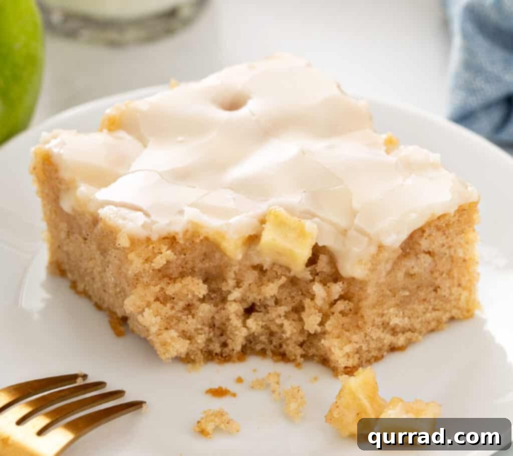 Autumn Apple Caramel Slab 5 A square piece of caramel apple sheet cake, with a bite taken, revealing the moist interior and apple chunks, resting on a white plate with a fork.