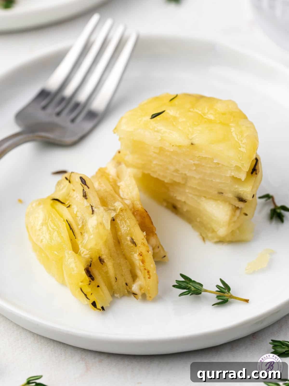 A stack of thinly sliced potatoes, baked with melted cheese, and cut in half on a plate to show the layers.