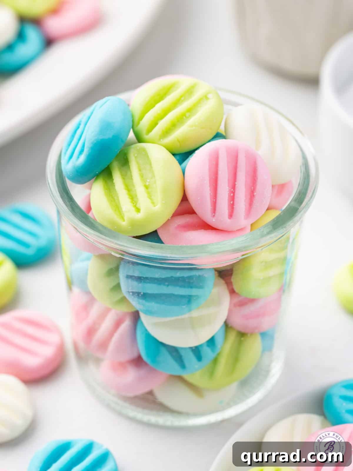 Velvety Mint Treats 2 A charming glass jar filled with an assortment of pastel-colored button-shaped cream cheese mints, showcasing their delicate appearance.