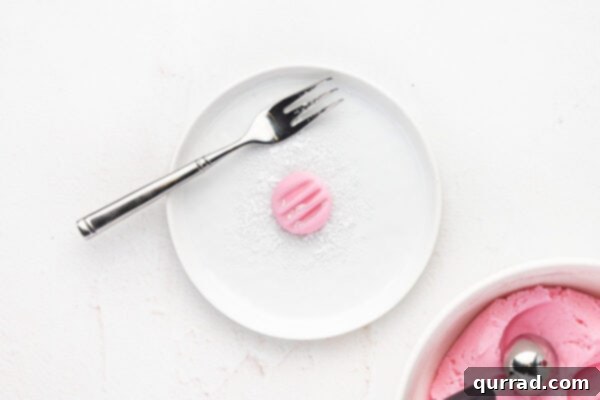 A pink cream cheese mint, freshly stamped with the distinctive pattern of fork tines, showcasing its ready-to-set appearance.