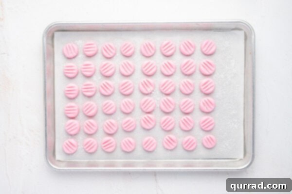 A baking tray neatly lined with rows of pink cream cheese button mints on parchment paper, allowing them to air dry and firm up.