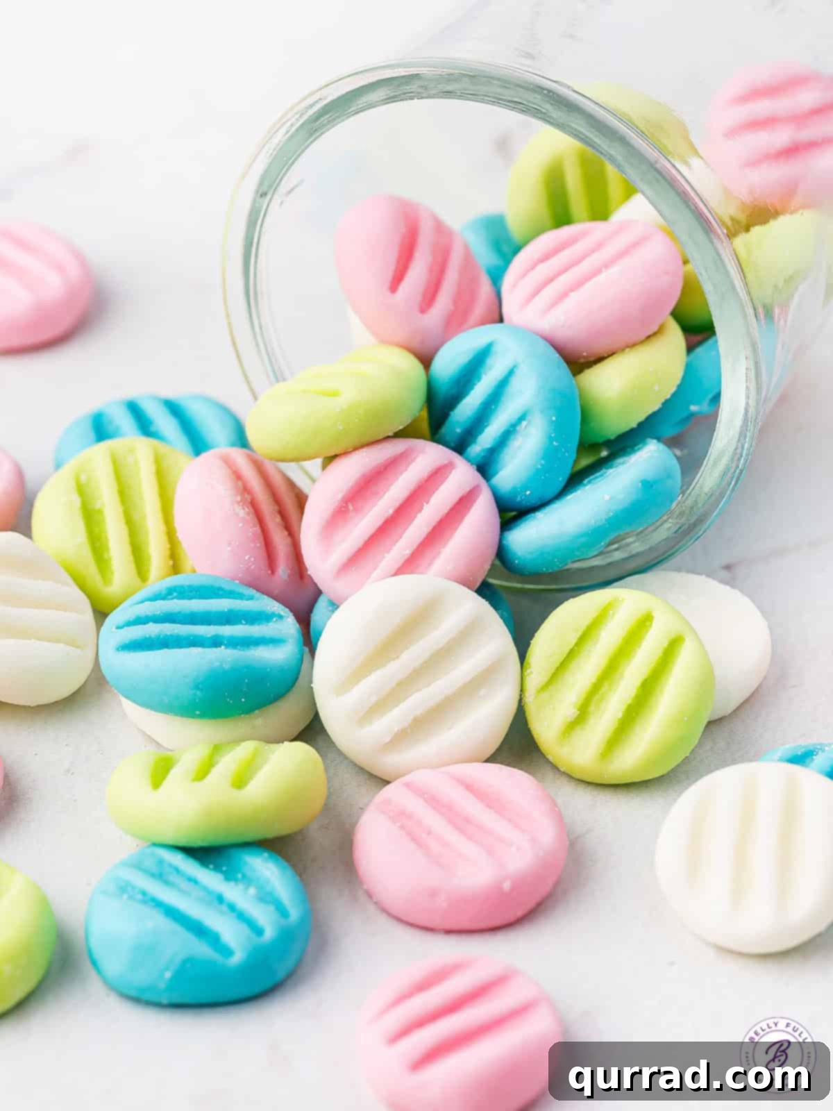 Velvety Mint Treats 4 Pastel-colored cream cheese mints, in shades of pink, blue, and green, gently spilling out of a clear glass jar, highlighting their delicate form.