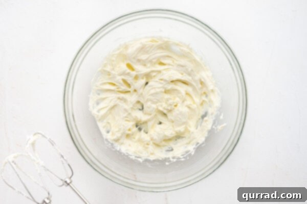 Whipped butter and cream cheese in a clear glass bowl, showcasing the smooth, creamy consistency before adding dry ingredients.